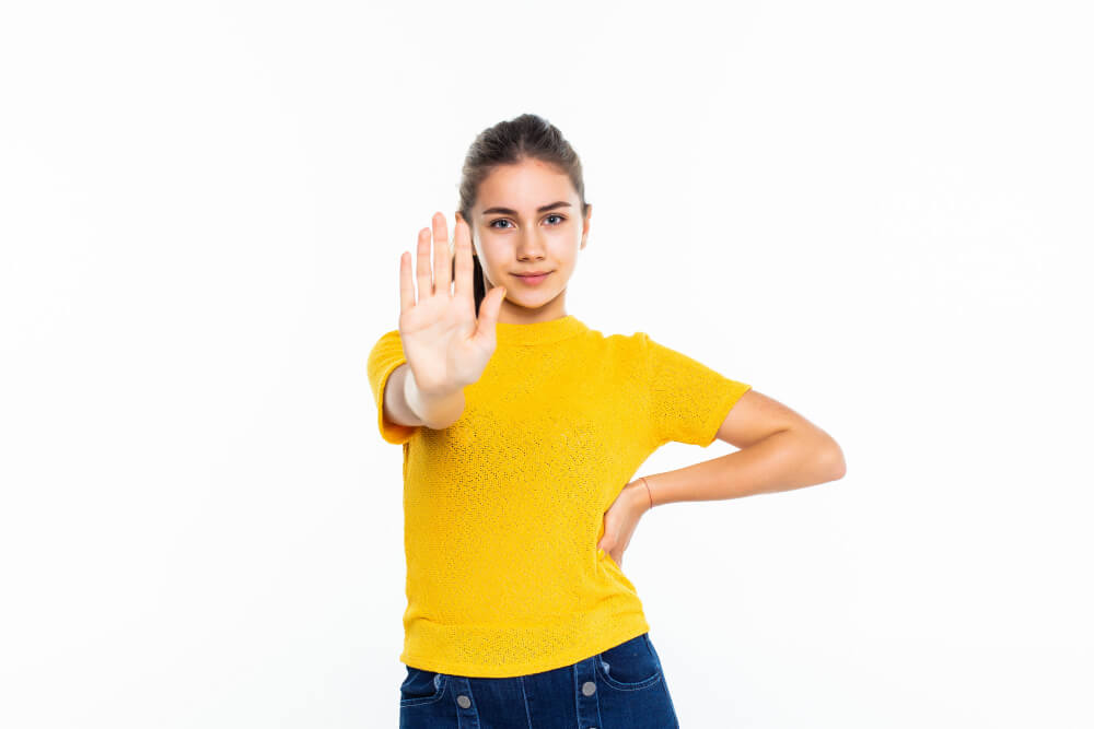 serious young teen girl in casual making stop sign on white wall