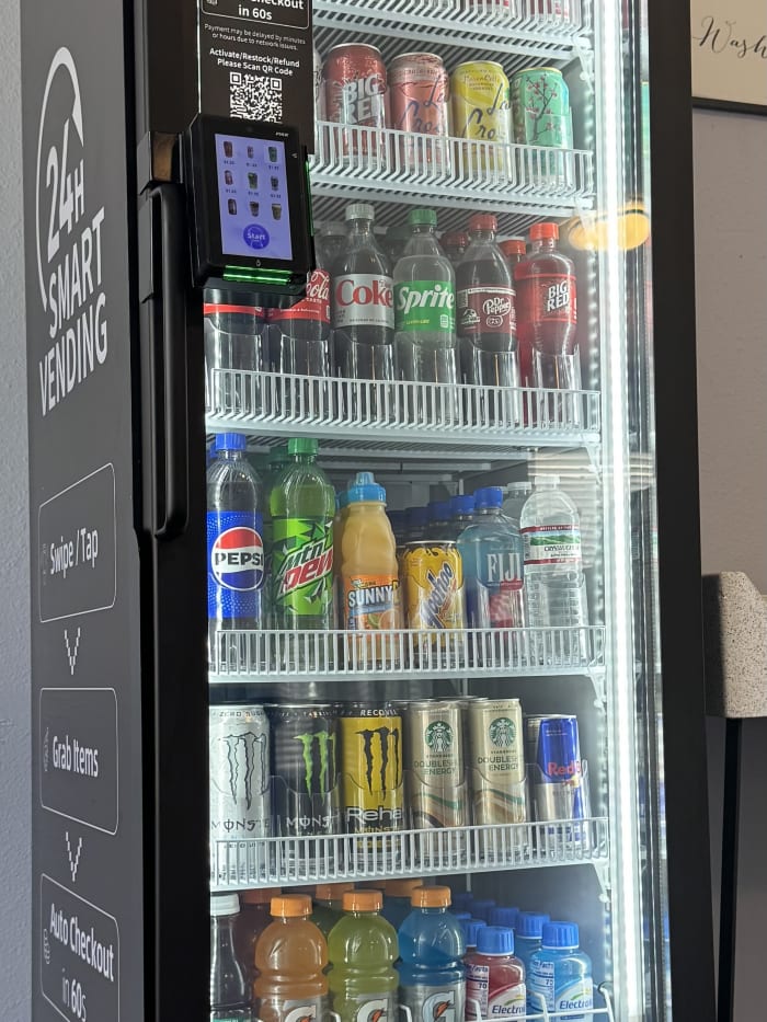 Three-quarter view of an installed managed micro market showing the side panel, the front glass with stocked product, and the tap-to-pay screen.