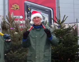 Adrian Bienias in working clothes and a Santa hat with a pruning shears against the background of Christmas trees