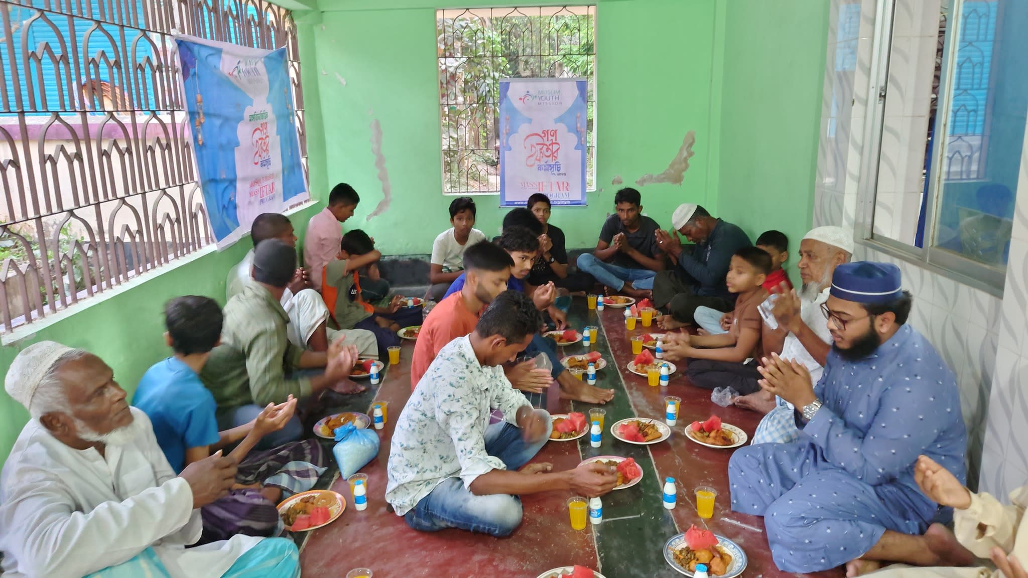 A group of people, mostly men, are gathered together in a colorful, open-air setting, sharing a meal and engaging in conversation.