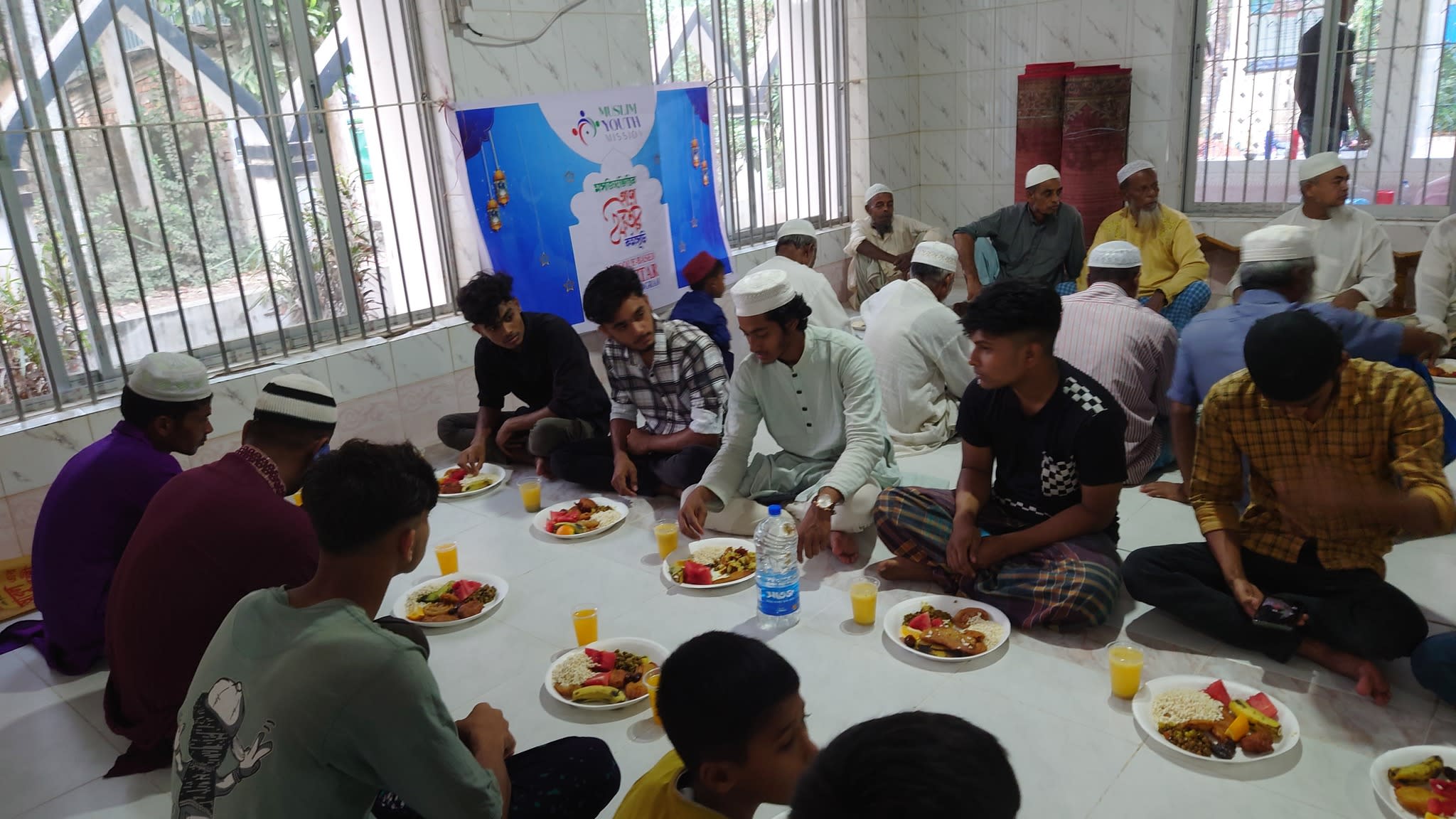 Several men are seated on the floor, appearing to be eating or having a meal together.