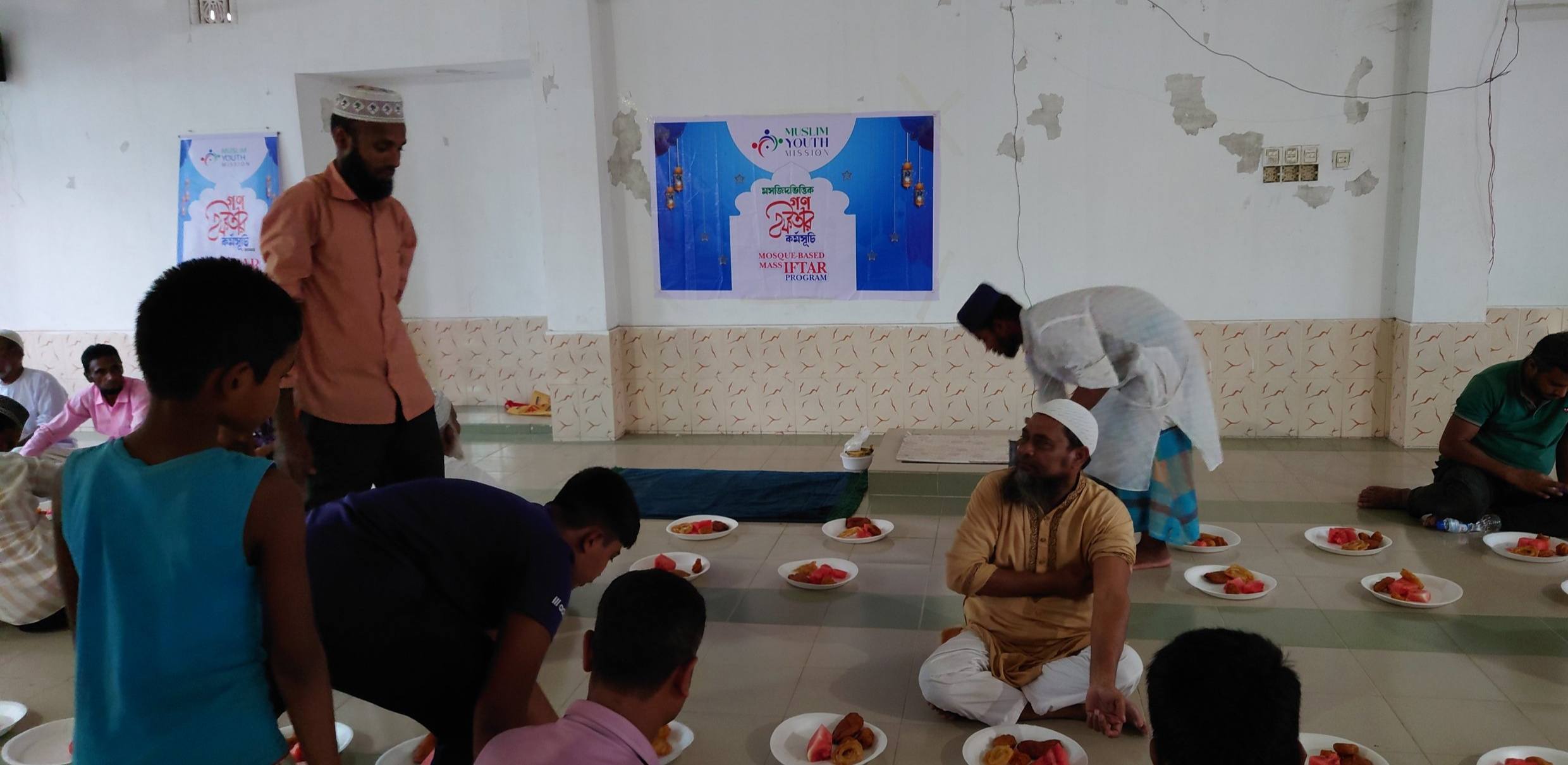 The image depicts a group of people gathered in what appears to be a religious or cultural setting, with individuals wearing traditional clothing and seated around a table with various dishes or offerings.