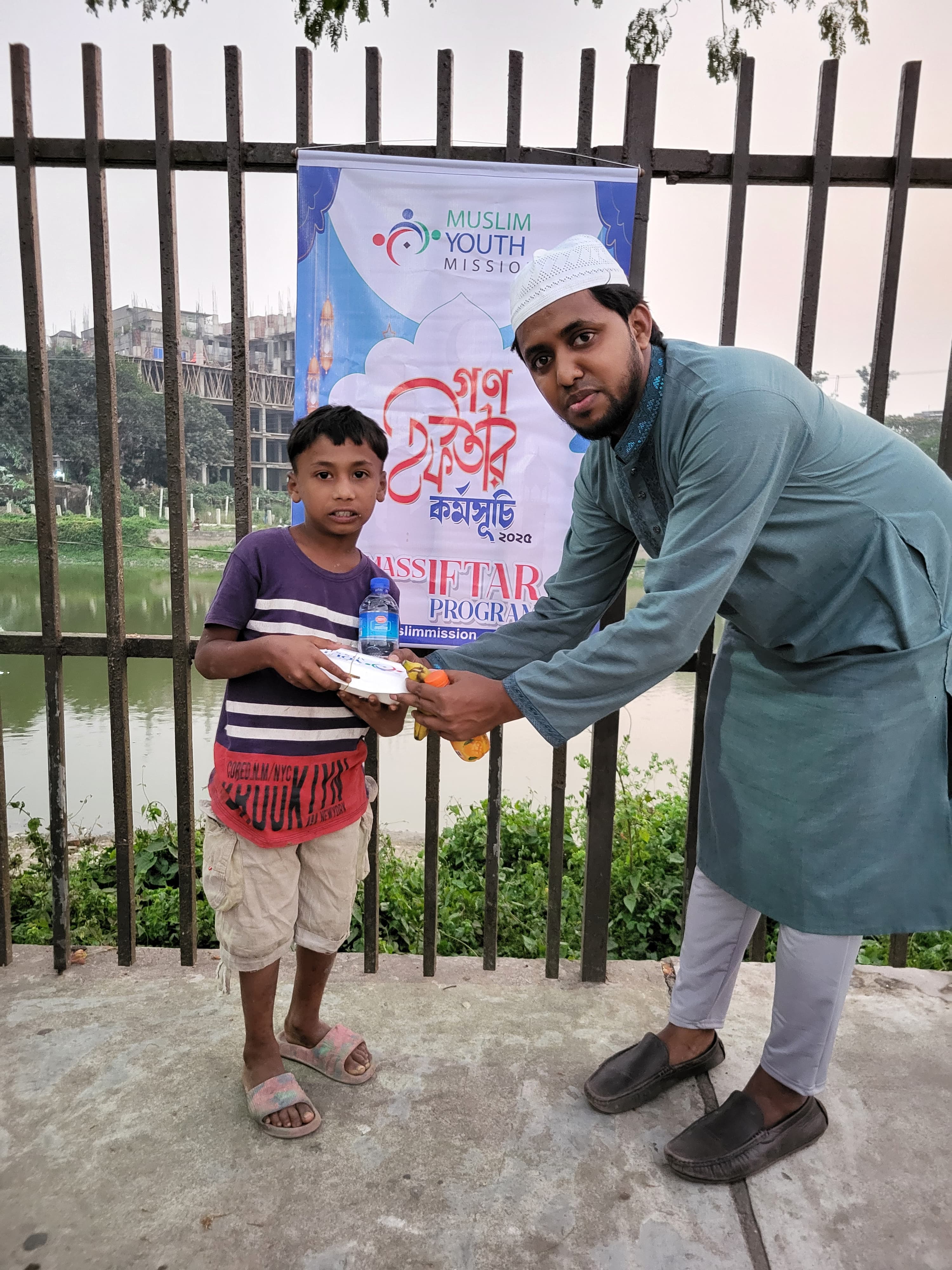 The image shows a man in traditional clothing interacting with a young boy in front of a banner for a Muslim youth organization.