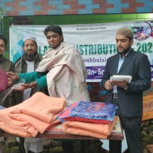 Multiple men receive blankets outdoors, likely during a distribution event.
