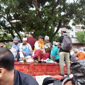 People on a makeshift boat during flooding; orange vests and debris visible in the background.