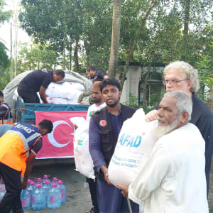 A man receives aid from volunteers during a delivery, with a Turkish flag in the background.