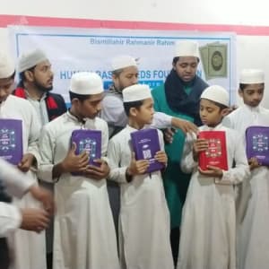 Several young men in white thobes and skullcaps hold books, likely in a classroom or study setting.