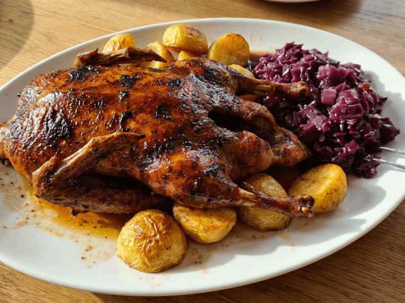 Whole roasted Czech duck with crispy skin, roasted potatoes, and braised red cabbage on a white oval serving plate.