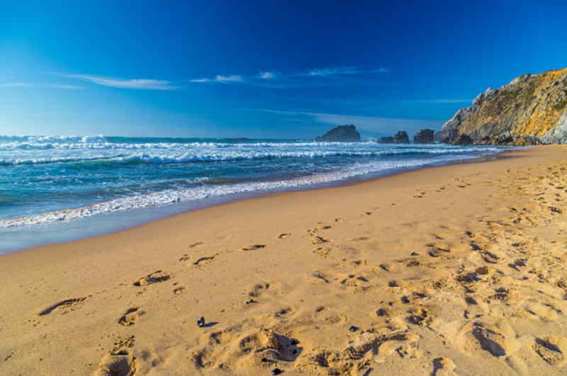 Footprints in the sand on a beach, with gentle waves lapping at the shore in the background.