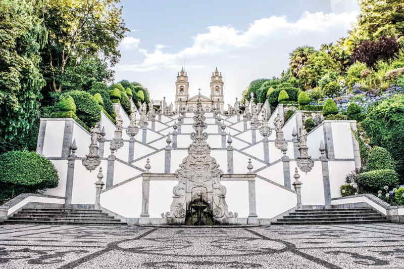Steps leading up to a white building, framed by greenery and sunlight, inviting visitors to enter.