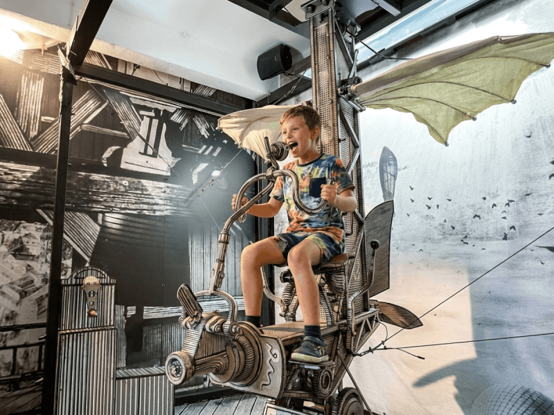 Boy laughing while sitting on an interactive flying machine exhibit at the Karel Zeman Museum in Prague.
