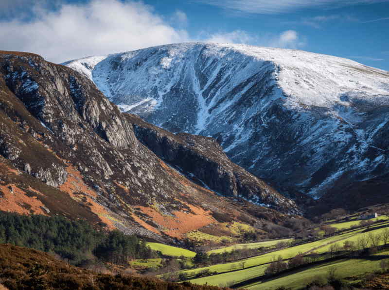 Snow-covered Lugnaquilla, the highest peak in the Wicklow Mountains, Ireland, rising above rocky slopes, colorful valleys, and green farmland