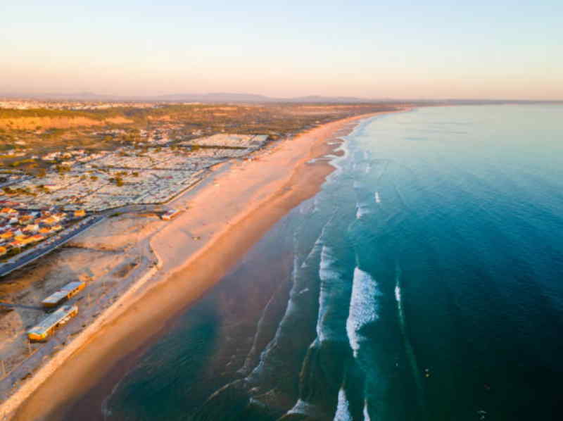 Aerial view showcasing a beach alongside a vibrant town, highlighting the coastline and surrounding buildings.