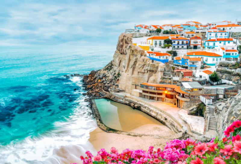 Scenic view of Algarve, Portugal, showcasing vibrant houses and blooming flowers against a clear blue sky.