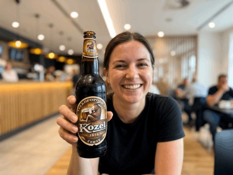 Woman smiling while holding a bottle of Kozel Dark, one of the best Czech beers, at a Prague bar.