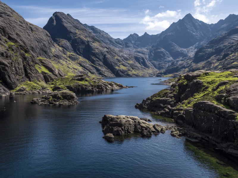 Loch Coruisk on the Isle of Skye, Scotland, with deep blue waters surrounded by steep rocky slopes and the jagged Black Cuillin mountains.