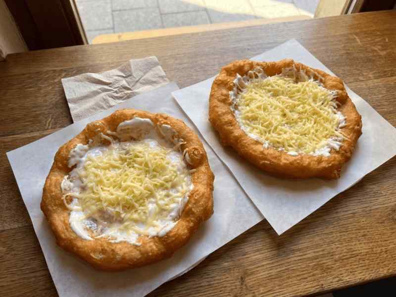 Freshly fried Hungarian lángos with sour cream and grated cheese on wooden table