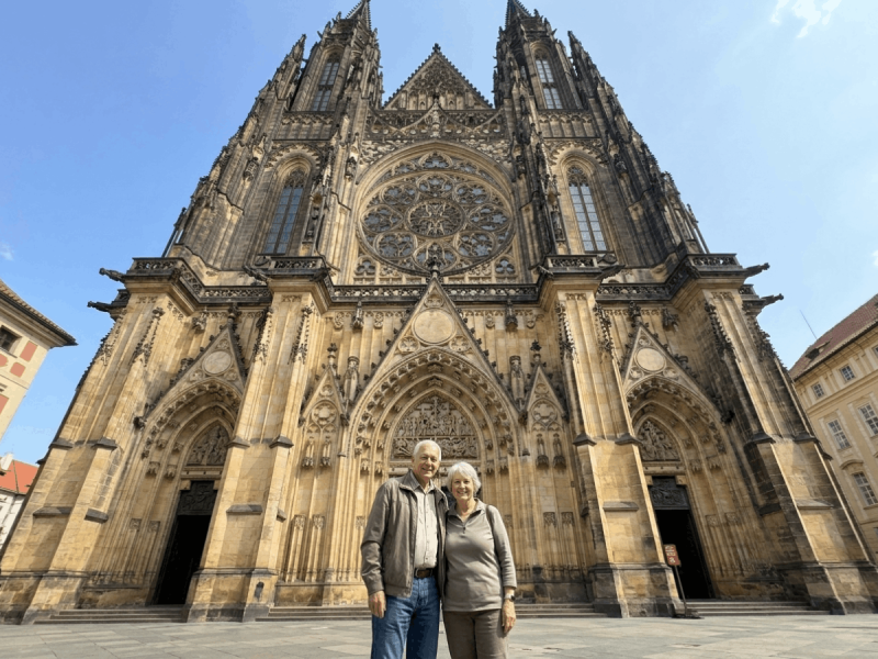 Couple standing before the twin spires and rose window of St. Vitus Cathedral's west facade, a Prague architecture landmark.