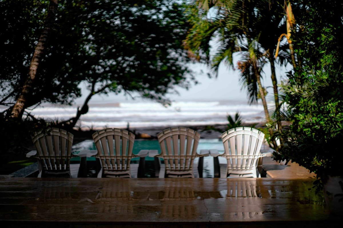 Raised teak bungalow at the edge of Costa Rican jungle, Pacific reef break visible offshore through palms, early morning light.