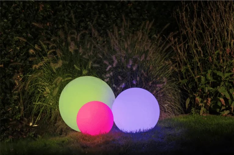 Boules lumineuses blanches disposées au sol sur une terrasse en bois pour baliser le contour.
