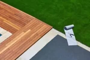 Espace détente extérieur mêlant une terrasse en bois exotique et un tapis de gazon synthétique.