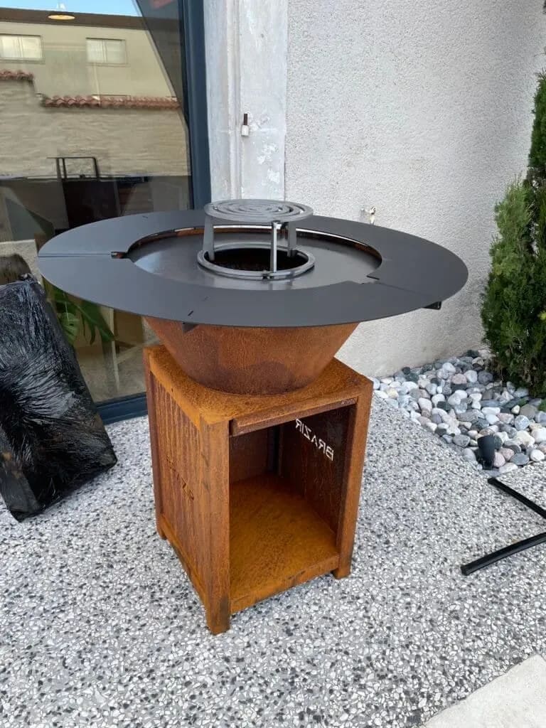 Brasero moderne avec ses accessoires disposés sur un aménagement extérieur en bois naturel.