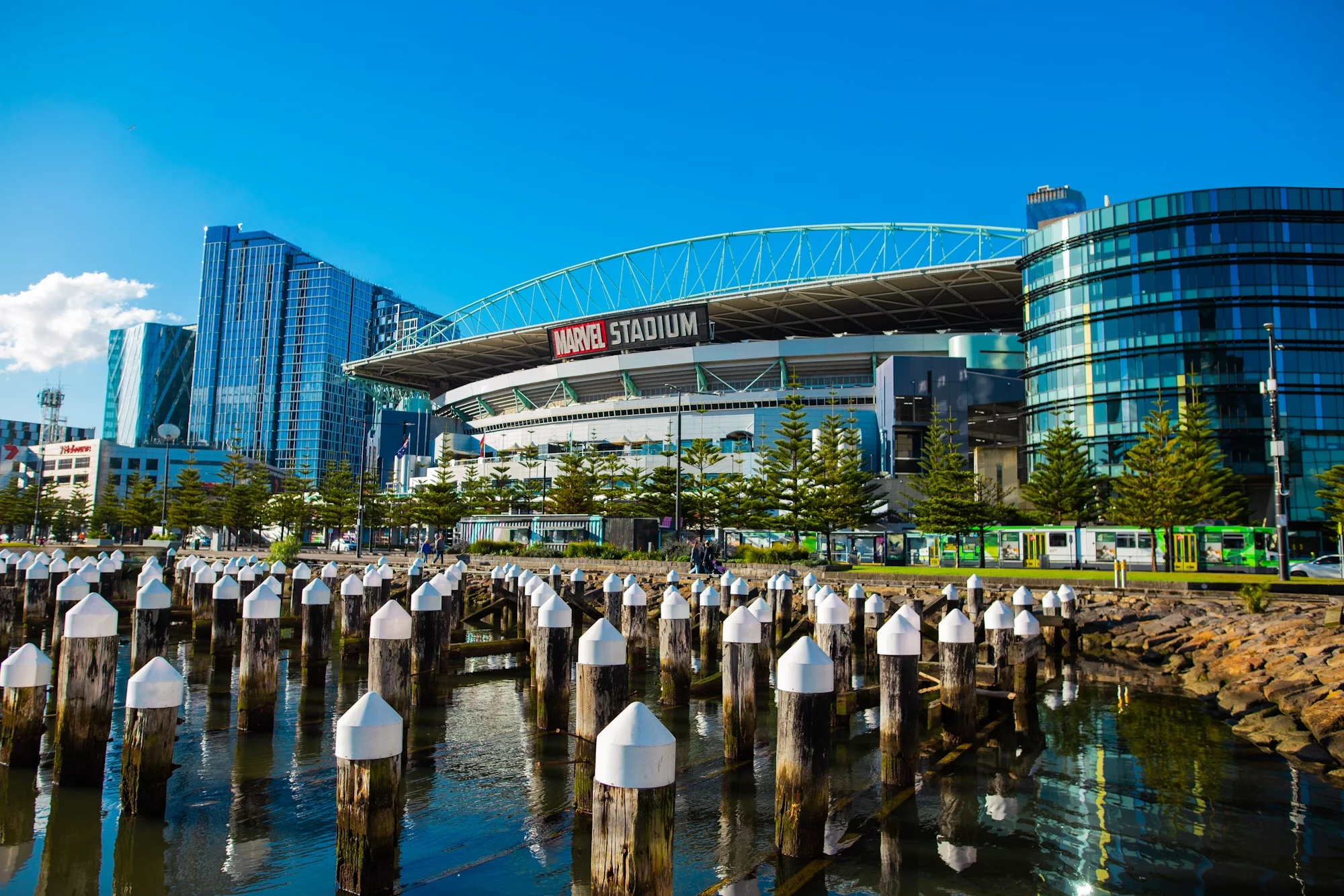 Marvel Stadium seen across the Docklands harbour, a tram passing in front