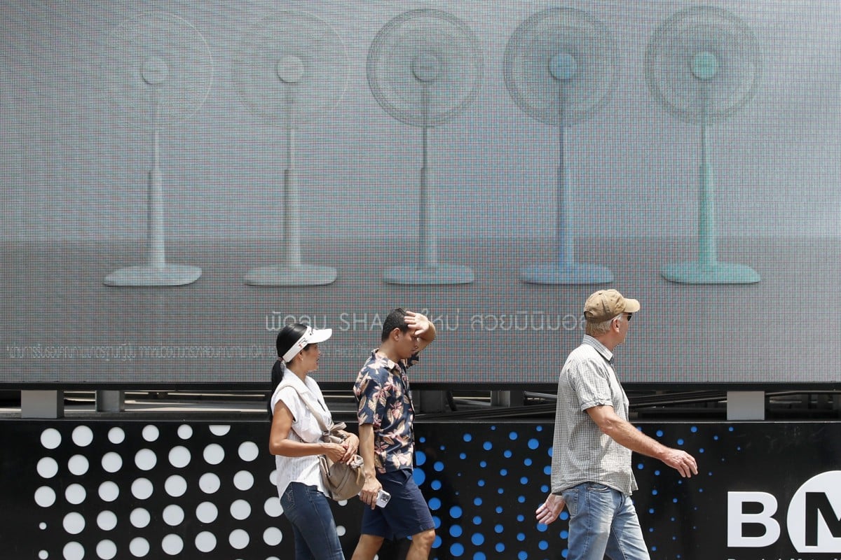 Pedestrians walk past an electric fan advertisement during hot weather in Bangkok, Thailand, 01 May 2024