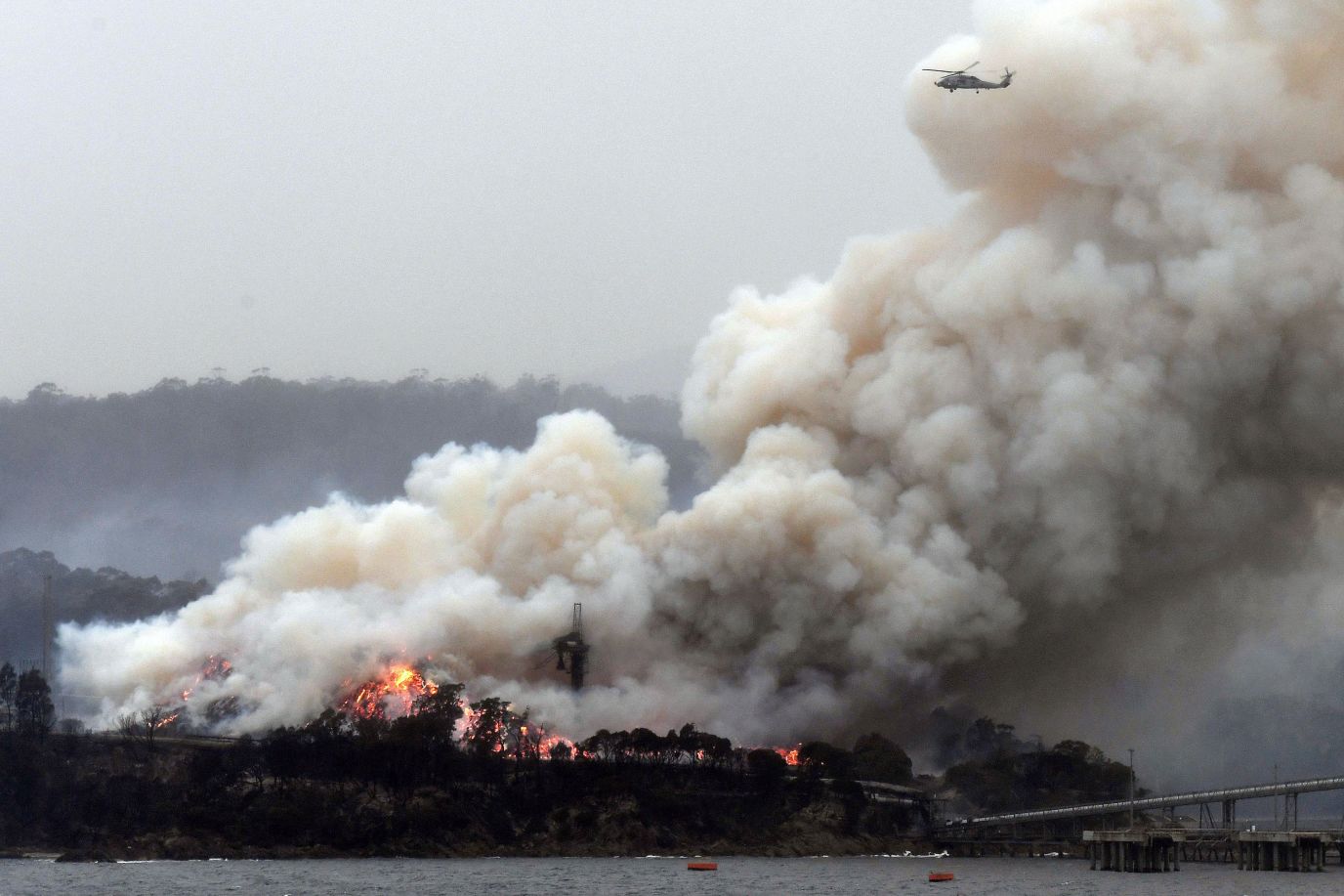 A military helicopter flies above a burning woodchip mill in Eden, New South Wales