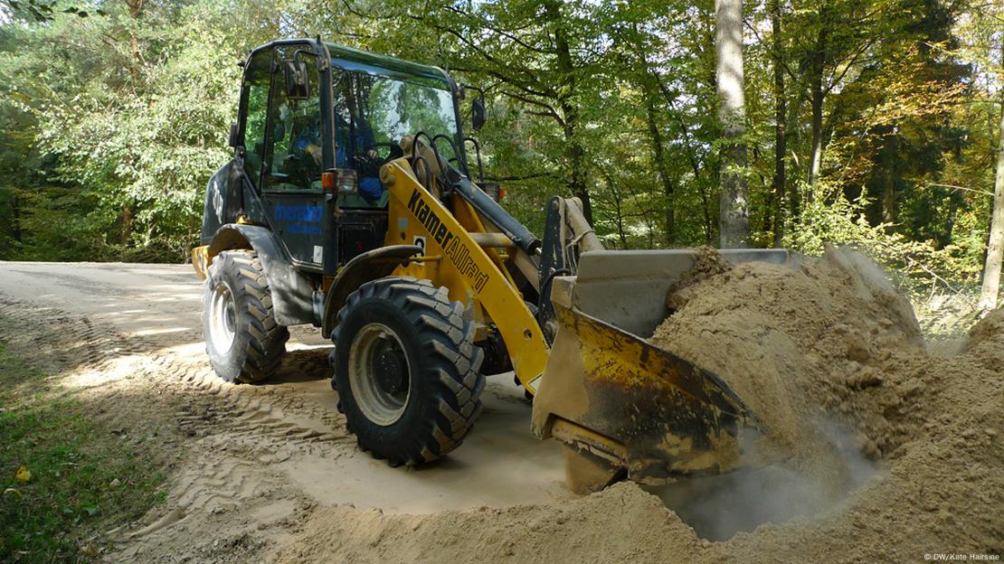 A bulldozer fills the bucket with a scoop of pulverized limestone and the chopper flies off with the yellowy colored powder trailing behind it.