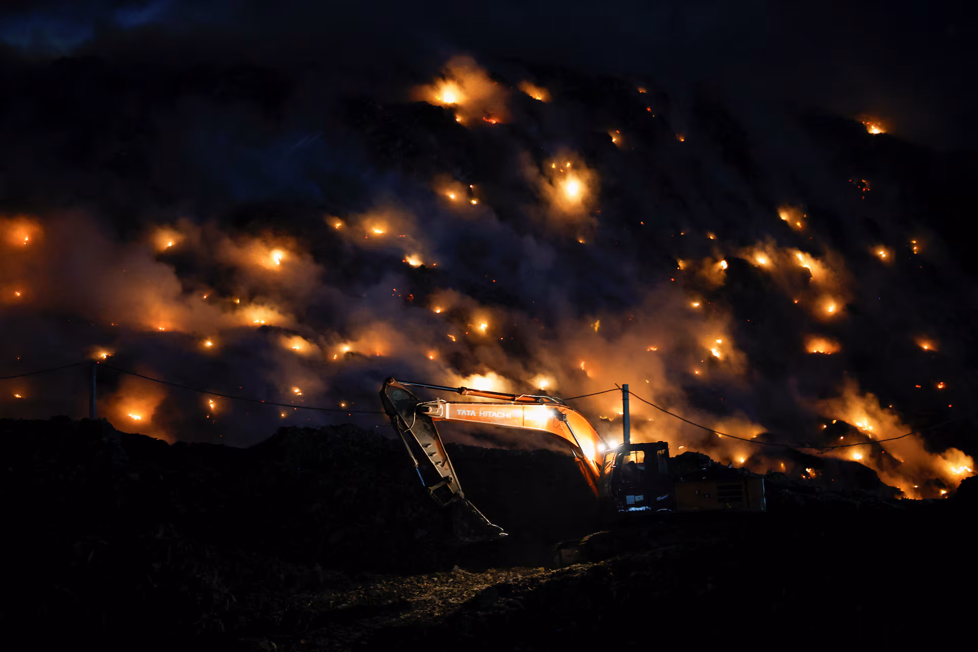 An excavator tries to contain the fire as smoke rises from burning garbage following a fire at Ghazipur landfill site in New Delhi, India