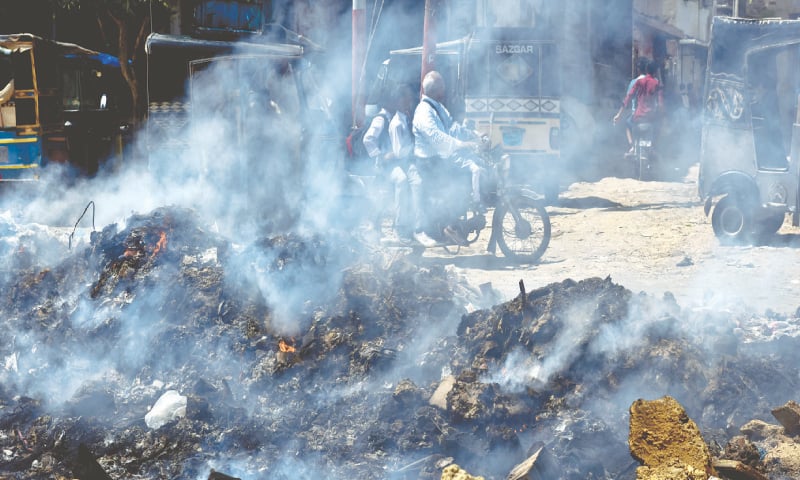 A motorcyclist rides past a burning pile of garbage. Karachi.