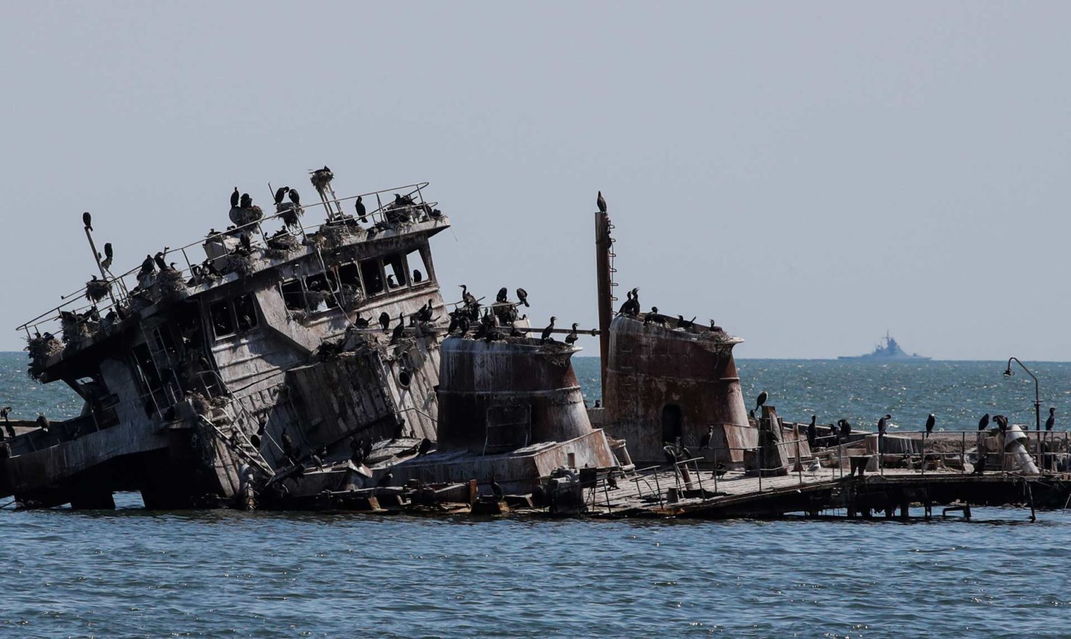 A Russian warship in the Sea of Azov behind a sunken Ukrainian ship in the cargo seaport of Mariupol, Ukraine, April 29, 2022. Ukraine's coastal and marine ecosystems have been impacted by chemical and acoustic pollution, physical damage to habitats.
