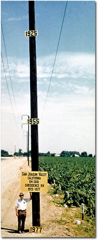 Signs on pole show approximate altitude of land surface in 1925, 1955, and 1977. The site is in the San Joaquin Valley southwest of Mendota, California