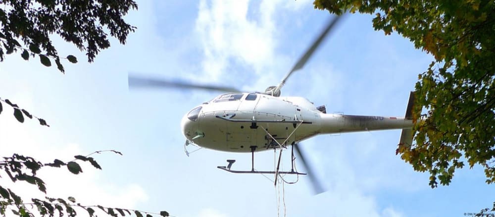 A helicopter hovers low over a patch of state forest near Kronau in southwestern Germany, swirling up leaves and dirt as it dangles down a 800 kilogram (1763 pounds) bucket tied on a piece of rope.