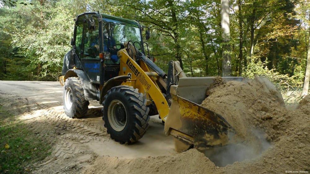 A bulldozer fills the bucket with a scoop of pulverized limestone and the chopper flies off with the yellowy colored powder trailing behind it.