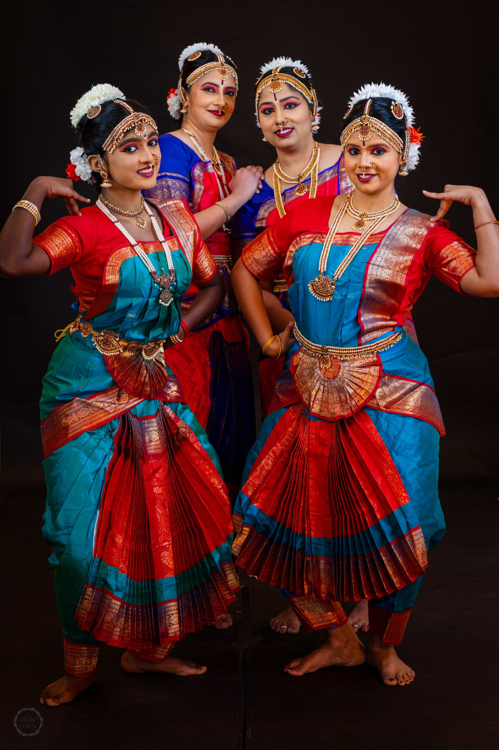 Four women in traditional Indian classical dance costumes posed against black background