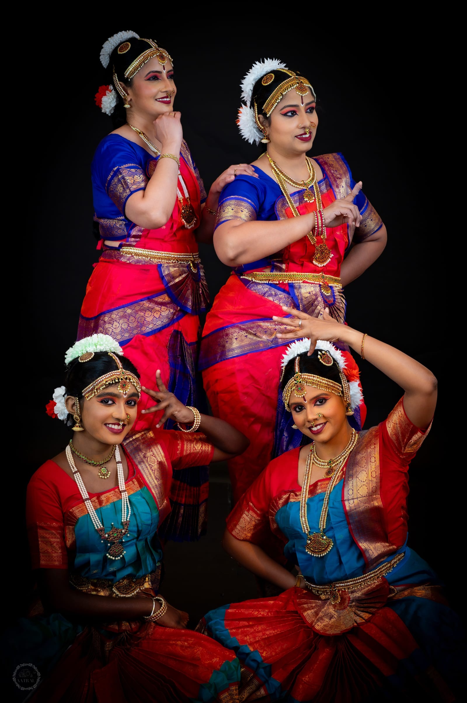 Four women in traditional Indian classical dance costumes against black background