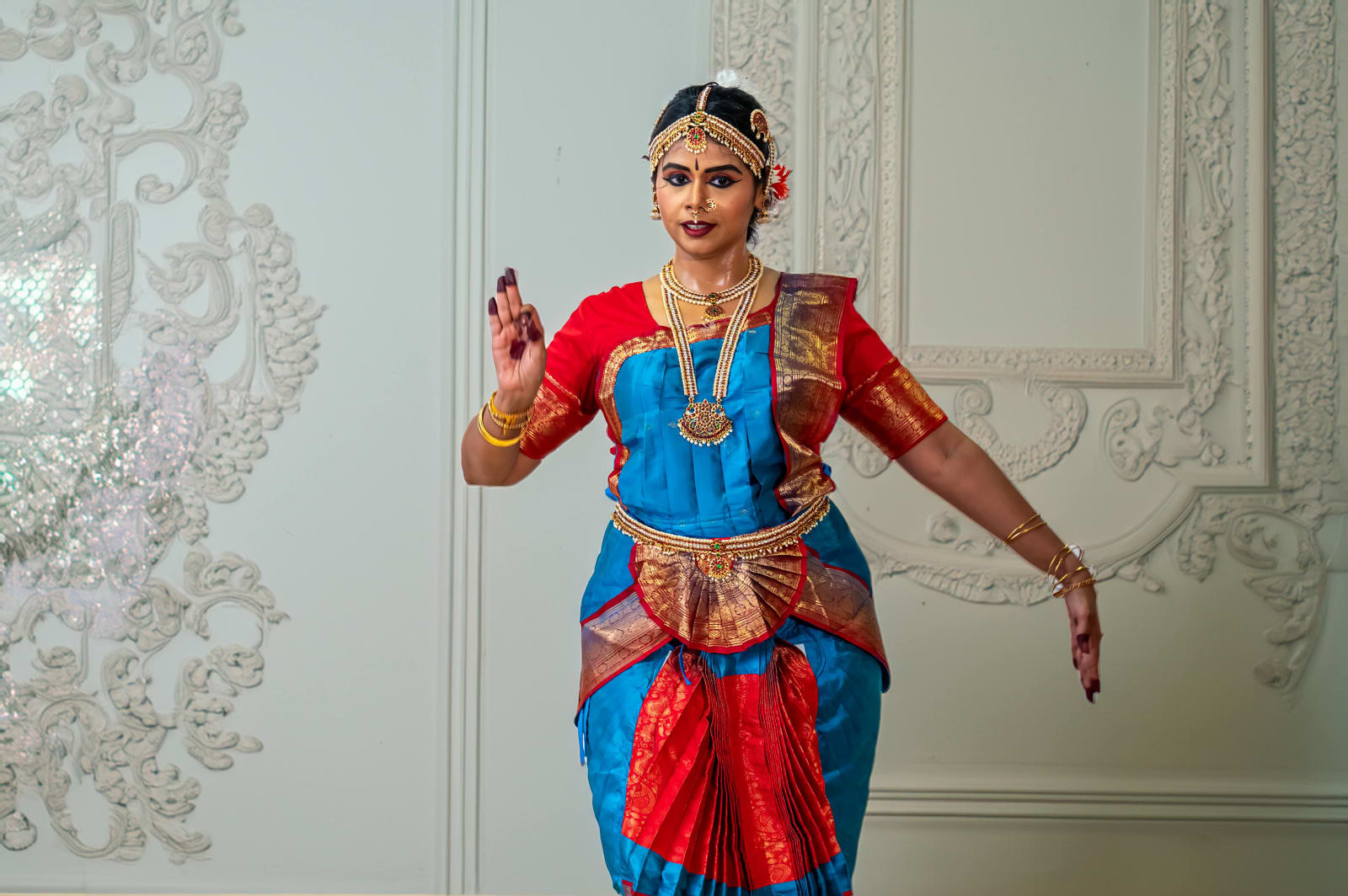Classical Indian dancer in traditional costume against ornate white wall