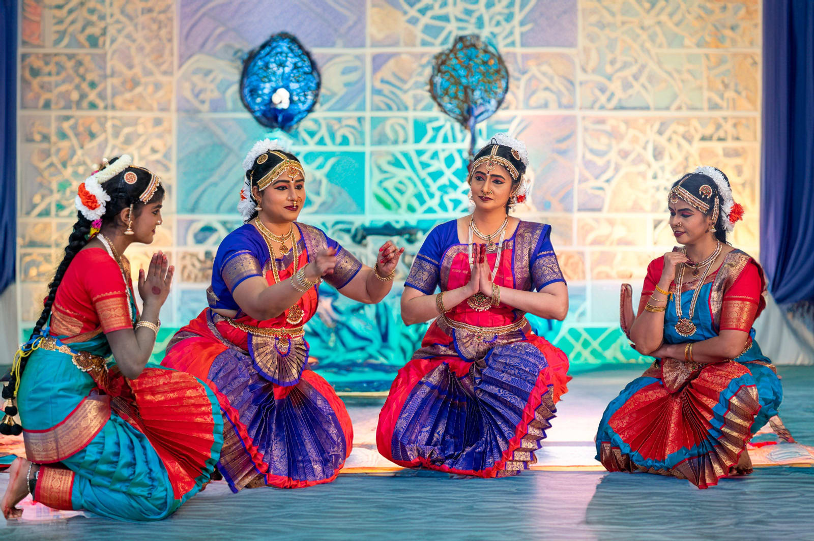 Four women performing classical Indian dance in traditional costumes on stage