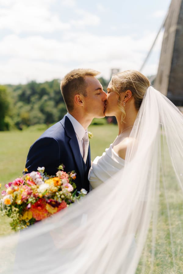 Bride and groom kissing by the Clifton Suspension Bridge, veil flowing