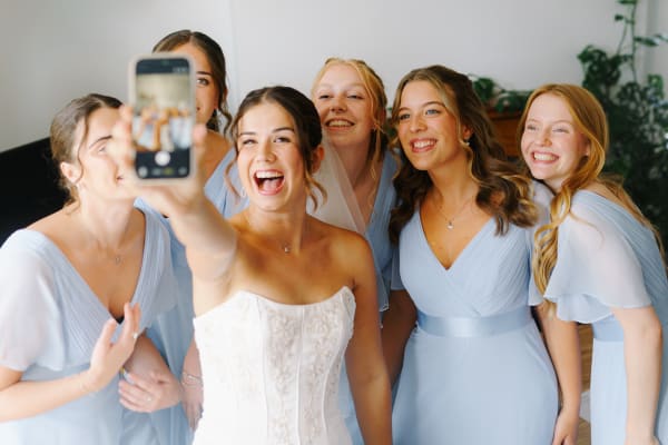 Bride taking a laughing selfie with her bridesmaids in pale blue dresses