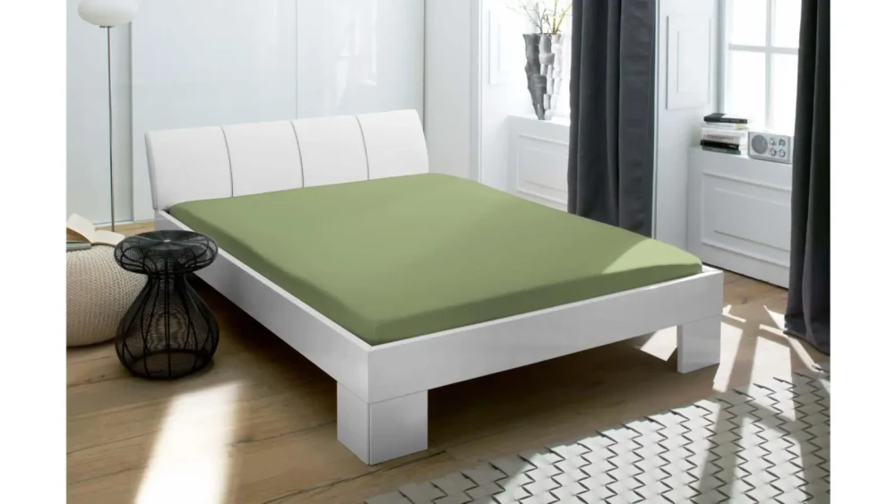 Schlafzimmer mit weißem Bett und grünem Spannbettlaken im modernen Design Modernes Schlafzimmer mit weißem Bettgestell, grünem Spannbettlaken, Holzboden und schwarzem Draht-Nachttisch