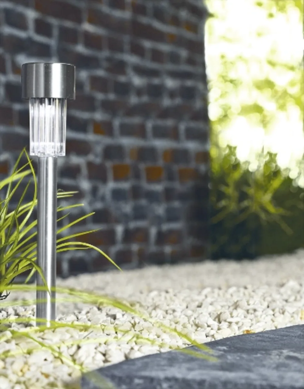 Solarleuchte im Garten Kleine Solarleuchte mit Edelstahlgehäuse und Lichtmodul in Steinbeet neben Rasen