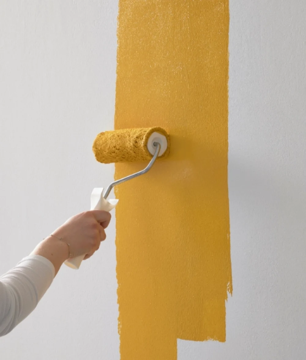 Farbrolle mit gelber Farbe Gelbe Wandfarbe wird mit Farbrolle auf weiße Wand aufgetragen