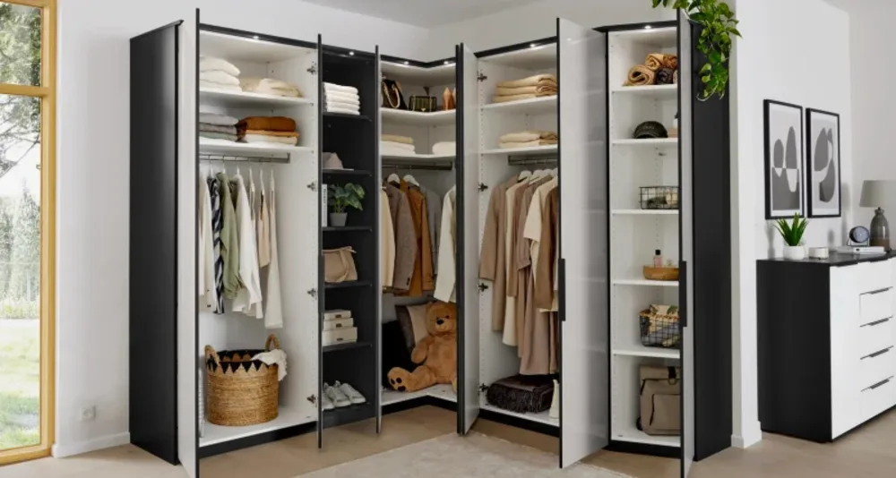 Kleiderschrank Geöffneter Eck-Kleiderschrank in Schwarz-Weiß mit LED-Beleuchtung, Kleiderstangen, Regalböden und ordentlich sortierter Kleidung.