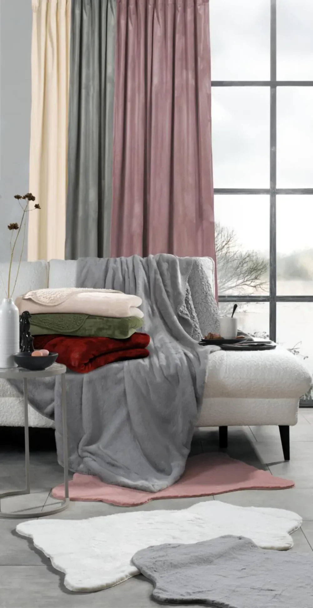 Wohnbereich mit Kuscheldecken und Vorhängen in sanften Farbtönen Couch mit flauschigen Decken in Creme, Grün, Rot und Grau, vor bodenlangen Vorhängen in Beige, Grau und Rosa