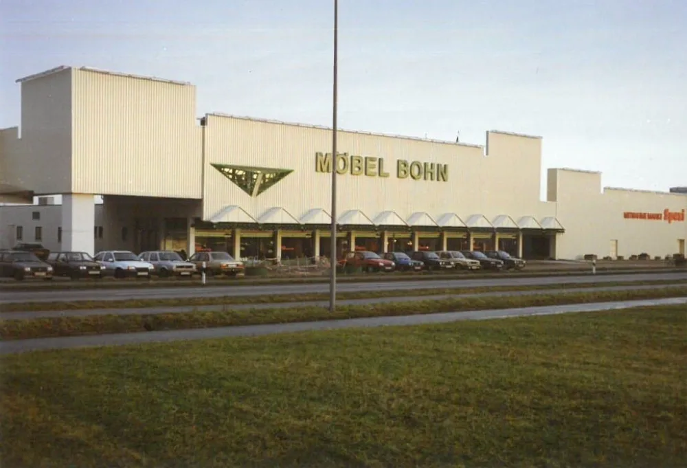 Hauptgebäude von Möbel Bohn mit Parkplatz früher. Außenansicht des früheren Möbel-Bohn-Gebäudes mit auffälliger Fassade und Parkplatz.