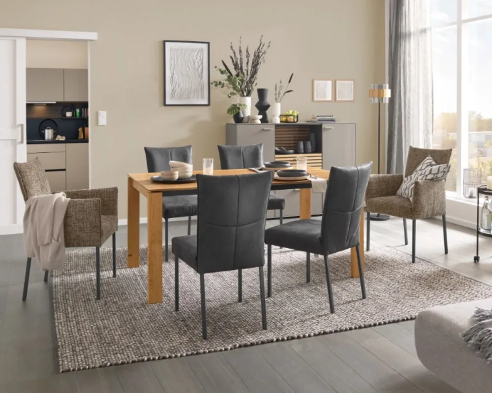 Zeitloses Esszimmer mit Massivholztisch, grauen Stühlen und wohnlicher Dekoration auf gemütlichem Teppich. Essgruppe mit Massivholztisch, gepolsterten Stühlen in Grau und Dekoration auf Teppich in modernem Wohnambiente