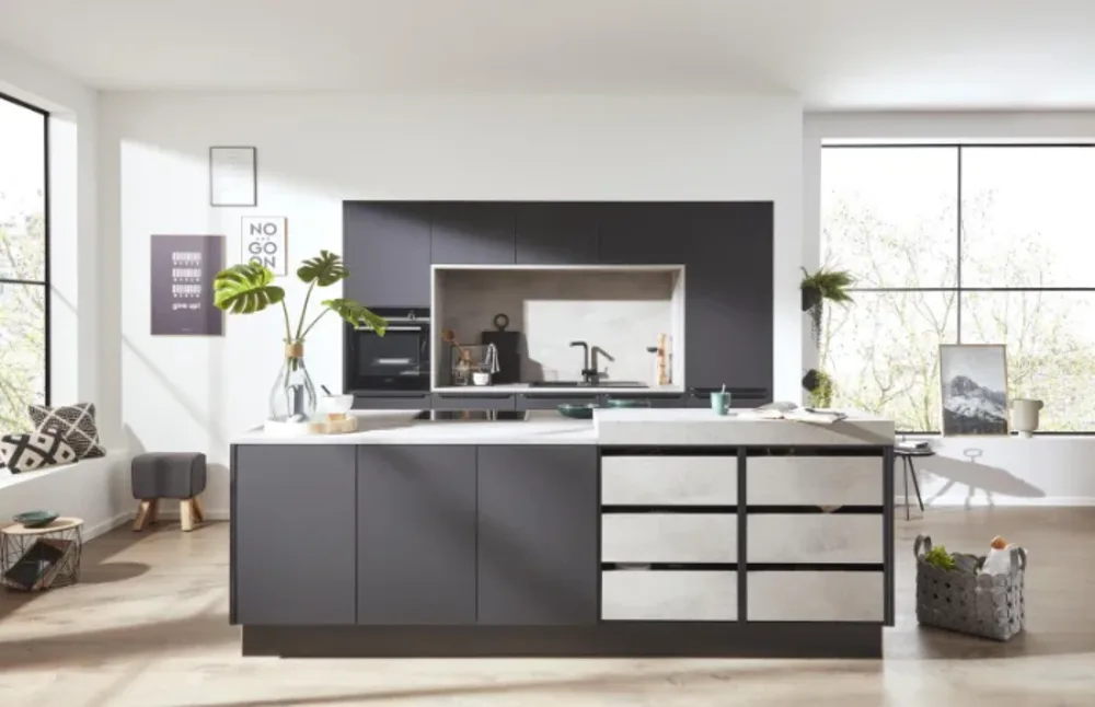 Schwarze Inselküche Designküche mit dunklen Fronten, heller Marmoroptik, Kochinsel und integriertem Spülbereich vor großen Fensterflächen.